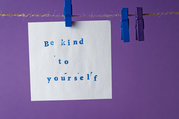 Be kind to yourself text written with rubber stamp font on a hanging paper.