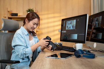 Asian woman holding a camera and using application video editor works on the computer with footage on wooden table. - 726435246