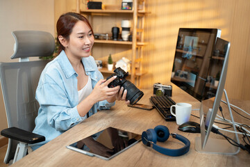 Asian woman holding a camera and using application video editor works on the computer with footage on wooden table. - 726435273