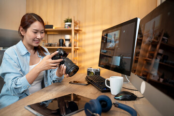 Asian woman holding a camera and using application video editor works on the computer with footage on wooden table. - 726435280