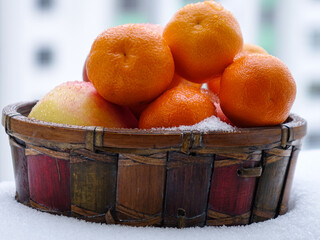 Wicker basket with tangerines and apple stands on the balcony on a winter day