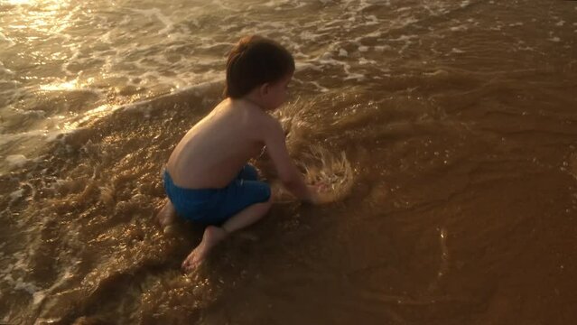 Kid having fun running barefoot along ocean coast at sunset.