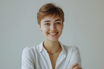 A woman wearing a white shirt with a pleasant smile, confidently posing with her arms crossed. Suitable for business, corporate, and professional themes