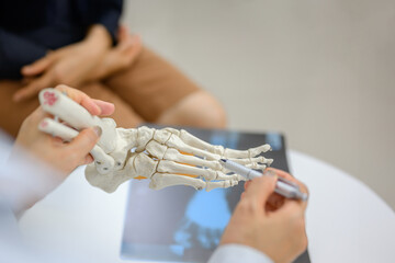 An orthopedic doctor points to a model of ankle and foot bones explaining to a patient a foot bone problem. Health care and spine concept