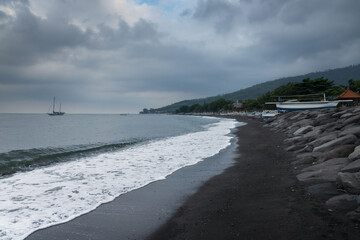 Black sand beach, fihsermen, boats and overcast sky at coastline of touristic Amed village in Bali...