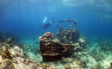 a woman diving and a small sunken boat on a reef in Curacao