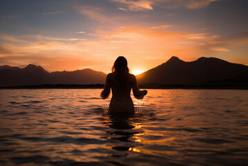 Fototapeta premium Back view of female silhouette in rippling water and enjoying sunset, in summer.