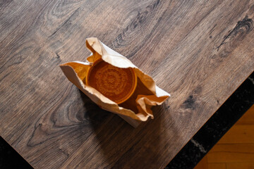 Tomato soup in a paper package on a wooden table. Paper bag. Takeaway food. Plastic cap. Lunch delivery