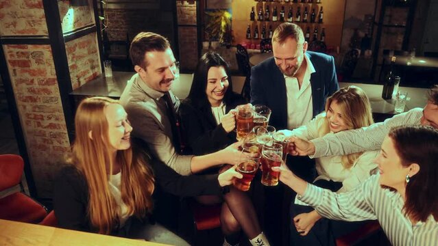 Saying toast and clinking glasses. Group of people, men and women meeting at pub, celebrating event, droning lager beer and having good time. Concept of leisure time, fun and joy, youth, enjoyment