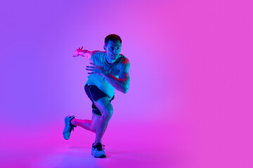 Fototapeta na wymiar Warming-up exercises. Sportive young man in sportswear training, doing exercises against gradient pink background in neon light. Concept of active and healthy lifestyle, sport, fitness, endurance