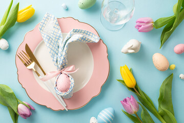 Celebrate Easter in style: Top view of a table featuring bunny ears napkin, small rabbit, cutlery, wine glass, tulips, sprinkles, and eggs. Pastel blue background adds a festive touch