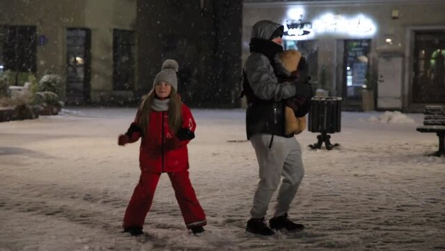 Dancing dad with baby kangaroo with two children and with a girl, father of daughter and son. Dancing on the street snow is falling on new year and christmas happy family