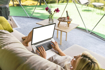 Woman working on laptop geo dome tents. Green, blue background. Cozy, camping, glamping, holiday, vacation lifestyle concept. Outdoors cabin, scenic background.