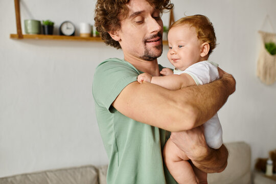 cheerful father with beard holding in arms his smiling infant son in a cozy living room, portrait