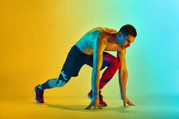 Ready to run. Muscular, sportive young man training shirtless against gradient blue yellow background in neon light. Concept of active and healthy lifestyle, sport, fitness, endurance