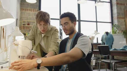 Professional female dressmaker teaching young male apprentice how to use sewing machine at work in atelier - Powered by Adobe