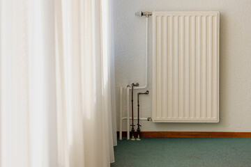 Old classic realistic white steel panel heating radiator, White sheer curtains hanging on the...