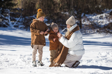 Fototapeta na wymiar Winter weekend. Mother and two sons in warm winterwear walking while having fun in winter forest among trees