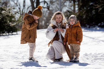 Fototapeta na wymiar Winter weekend. Mother and two sons in warm winterwear walking while having fun in winter forest among trees