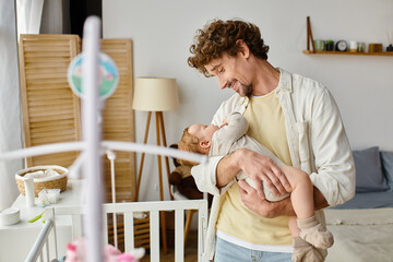 happy single father holding in arms his infant son near baby crib in nursery, fatherhood and love