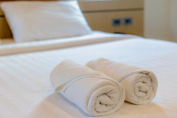 Fototapeta na wymiar Stacked of white fluffy and cleanliness towels on bed sheet, Freshly laundered folded towels in a roll in hotel bedroom, Decoration in bedroom interior.