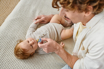 top view of curly and bearded father holding pacifier near infant baby boy on bed, fatherhood