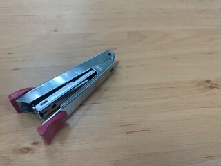 Paper stapler with pink handle on wooden table, office stationary 