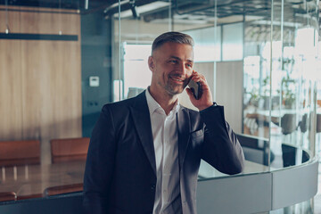 Handsome male manager in business casual clothes is talking phone with client at office 
