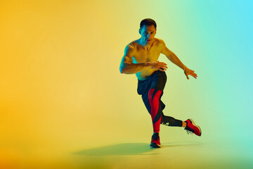 Shirtless male athlete in mid-action with focused expression training shirtless against gradient blue yellow background in neon. Concept of active and healthy lifestyle, sport, fitness, endurance