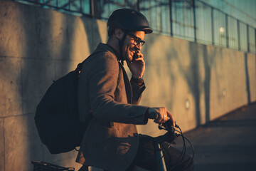 A side profile of a happy businessman with a backpack making a phone call and sitting on a bicycle.