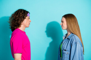 Side profile photo of furious couple teenage boyfriend looking at his girlfriend grimacing isolated on aquamarine color background