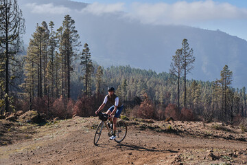 Fototapeta premium Male cyclist riding a gravel bicycle a gravel road through burned forest on Tenerife, Canary Islands, Spain. Sport motivation. Cycling training outdoors in Spain. Cycling adventure .