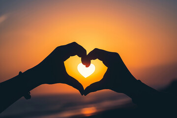 Silhouette of hands forming a heart shape against the backdrop of a sunset