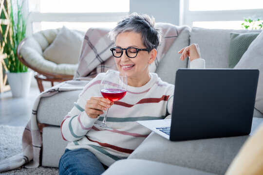 Photo of cheerful peaceful grandmother hold wine glass watch movie laptop spend pastime modern flat inside - Powered by Adobe
