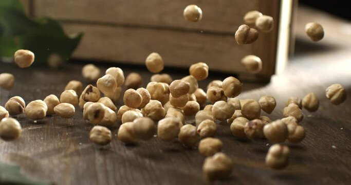 Super slow motion macro of fresh bio organic peeled dried hazelnuts are falling on wooden rustic table in kitchen of restaurant at 1000 fps.