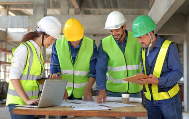 engineering teamwork wearing full safety gear discussing with blueprint and laptop on table in a new building under construction,engineers project manager consultation meeting with coworker