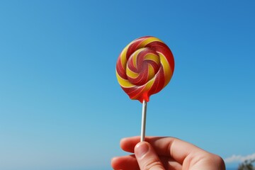 hand holding lollipop against clear blue sky
