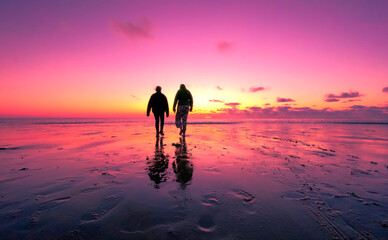This captivating image showcases the silhouettes of a couple walking hand in hand along a vast beach, with the afterglow of the sunset painting the sky in shades of purple and pink. Their reflection