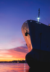 Silhouette forward side of oil tanker ship moored at harbor against colorful sunset sky background...