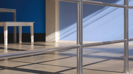 Sunlight and shadow on surface of stainless steel fence on beige tile floor of resting area, street minimal architecture background