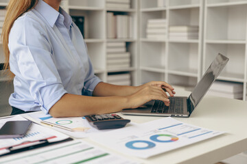 Close-up of business woman or accountant working using laptop computer to analyze business report graphs and financial charts to check company finances, income and monthly expense budget.