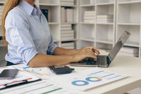 Close-up of business woman or accountant working using laptop computer to analyze business report graphs and financial charts to check company finances, income and monthly expense budget.