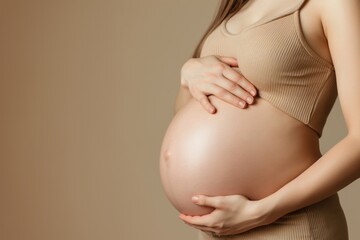 9 month pregnant woman touching belly against beige background with copy space