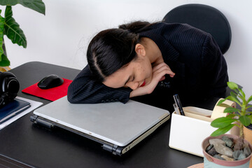 Overworked young female office worker asleep at her desk, showing fatigue with a closed laptop in...