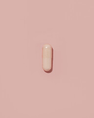 Top view of vitamin pill on pastel pink background with shadow