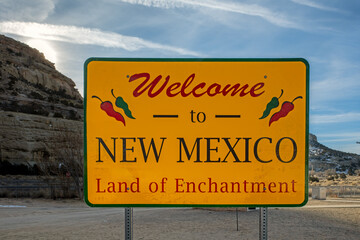 Welcome to New Mexico road sign with an overcast sky and mountains in the background.