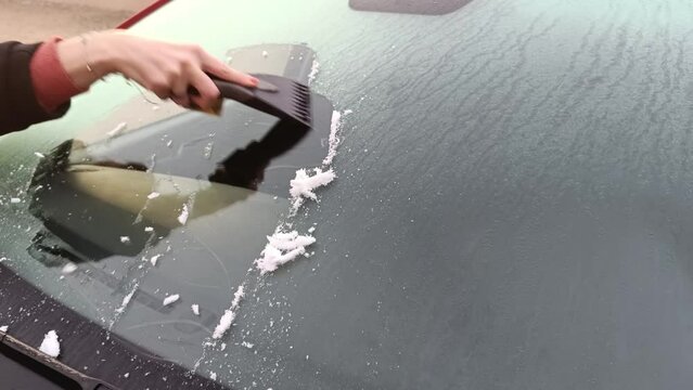 main d'une femme grattant la glace sur le pare-brise d'une voiture