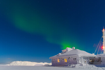 Northern lights, aurora, on top of a mountain, view of the night starry sky. Winter landscape . The building is covered with snow and frozen
