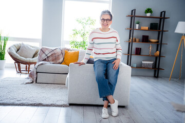 Photo of adorable pretty woman dressed striped sweater eyewear sitting couch smiling indoors house...