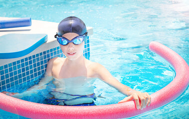 Happy child (boy) in cap, sport goggles ready to learns professional swimming with swim noodles and...